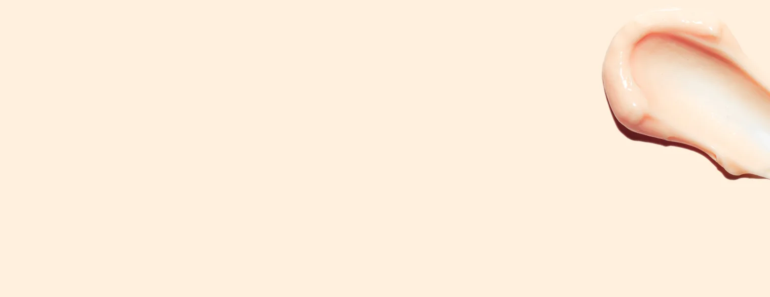 Makroaufnahme einer Cremetextur auf der Haut vor warmem beige Hintergrund.