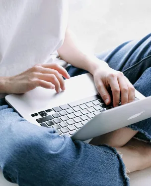 Person sitzt im Schneidersitz und tippt auf einem Laptop.